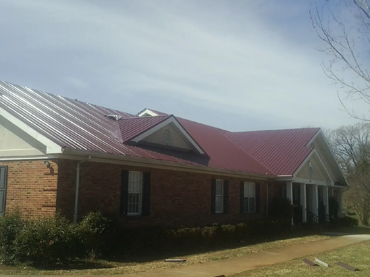 Red metal roof with gabled entries on a long brick building, from a Hail Damage Roof Repair job in Murchison